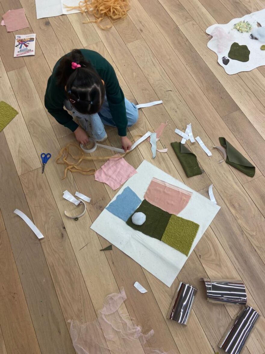 Child kneeling on the floor using tape, scissors and fabric to collage