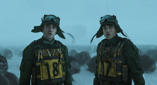 Two identical men stand side by side in hats and goggles. One has the number 18 on his front, the other has number 17.