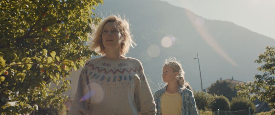 A woman walks in front of a young girl as the sun beams.