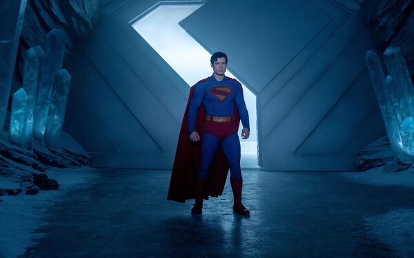 Superman stands in a blue lit room with ice and snow in the background. 