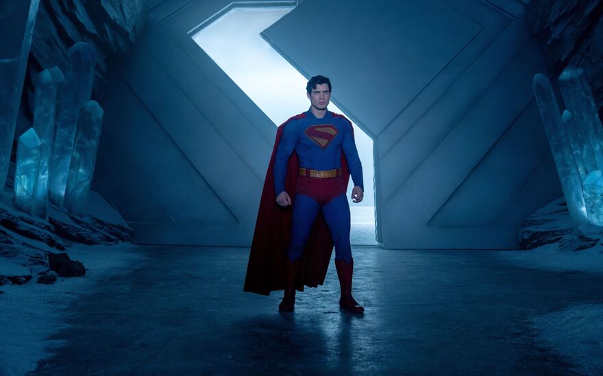 Superman stands in a blue lit room with ice and snow in the background.