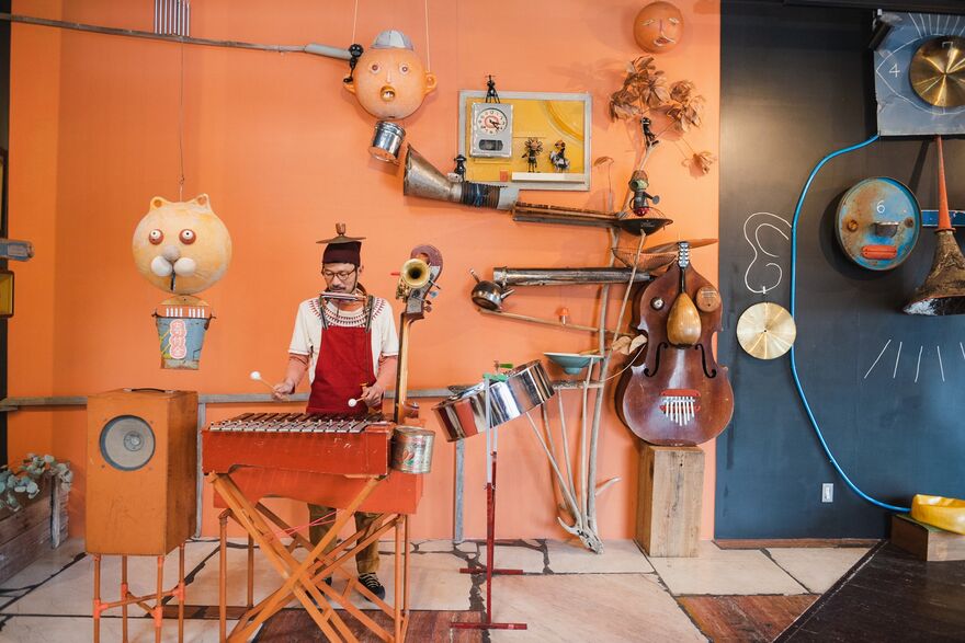 ICHI plays a xylophone surrounded by instruments 