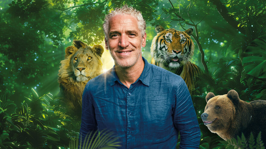 Gordan Buchanan in a blue shirt surrounded by trees and a bear, a tiger and a lion