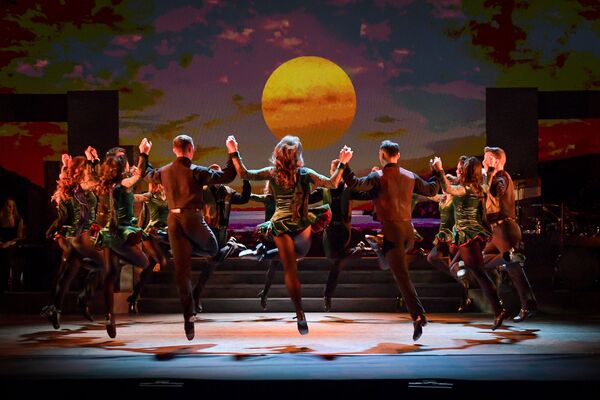 A group of dancers on stage. They hold hands in a circle as they dance. 