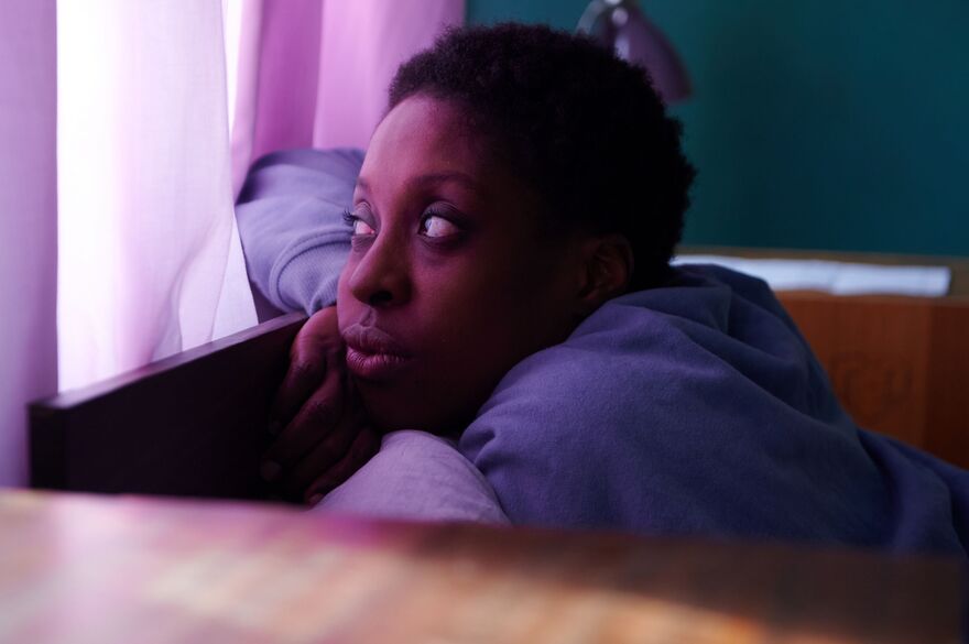 A woman leans against a headboard looking out a window. 