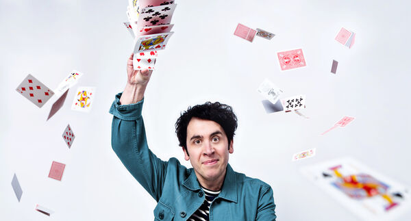 Pete Firman holding his arm up holding a pack of cards that are falling through the air