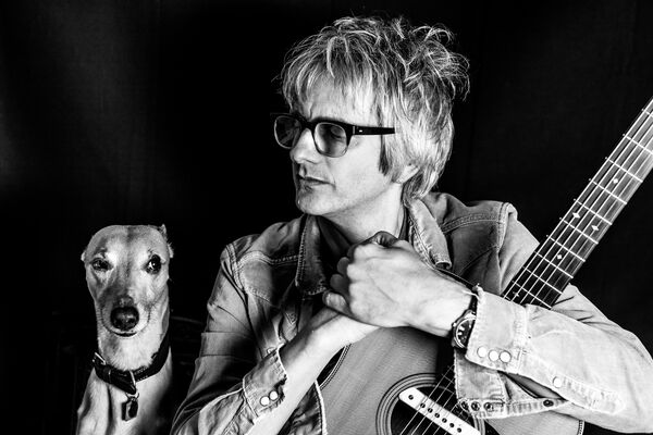 Nick Cope holding his guitar looking at his dog, imagge in black and white
