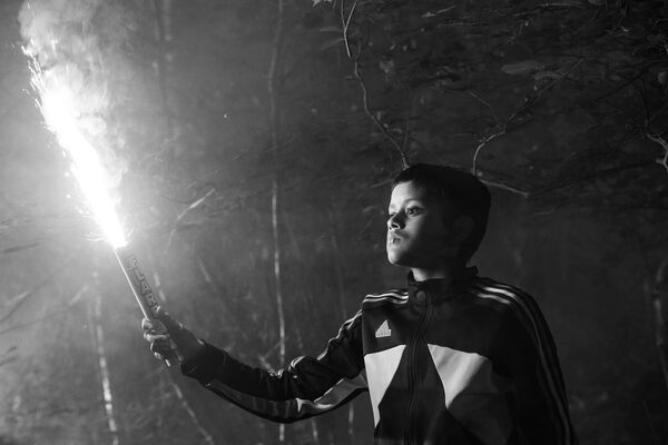 A black and white image. A young boy holds a lit flare. A black and white image. A young boy holds a lit flare.