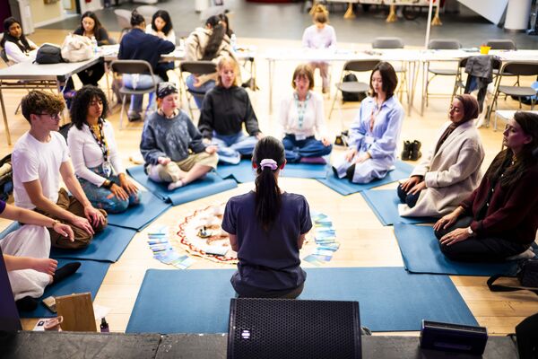 Group of Students and a Yoga teach sat on yoga mats in a semicircle