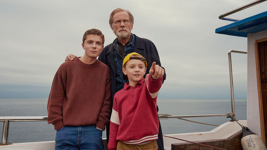 A grandad stands with his two grandsons on a boat.