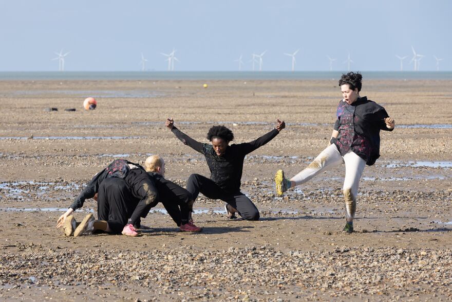Four people on the beach, one kick a ball, two on their knees and another laying on the back 