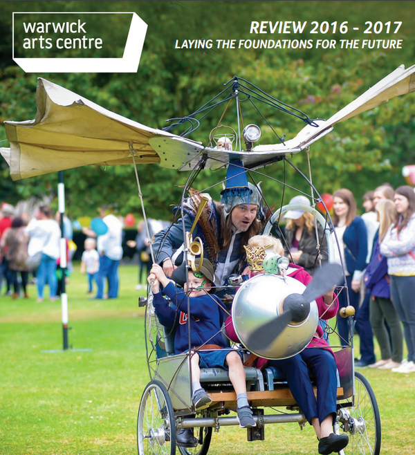 A bizarre flying machine rolling along some grass with a child in the front seat