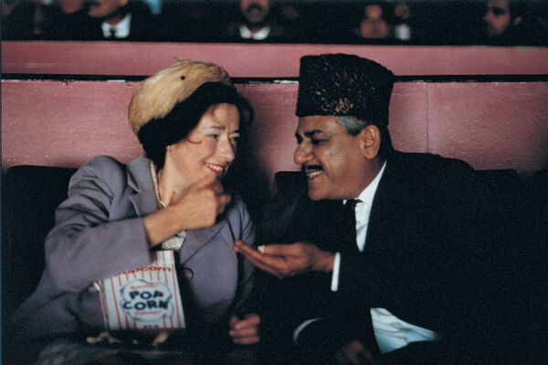 An older man and woman laugh together in a cinema as they eat popcorn. 