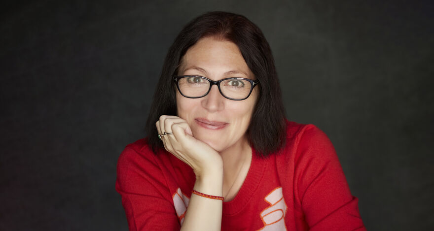 Natalie Haynes in a red jumper with a dark grey background