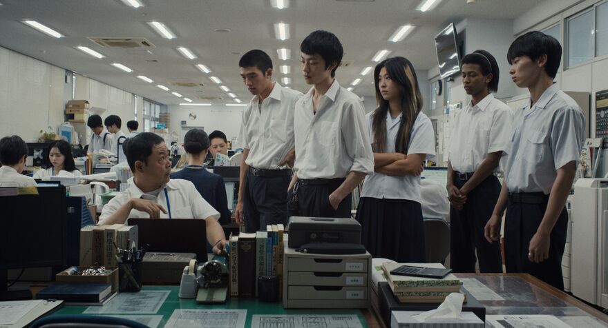A group of students stand around a desk.