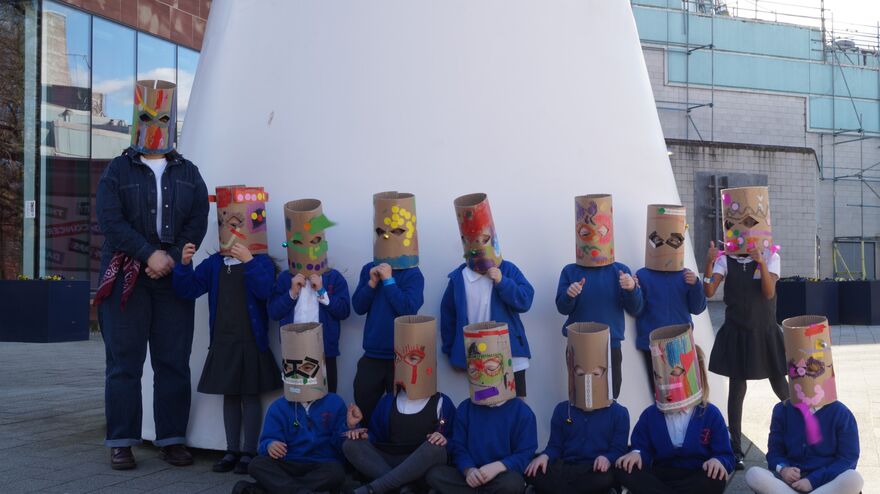 Children and a teacher stood in front of a large white sculpture with masks on 