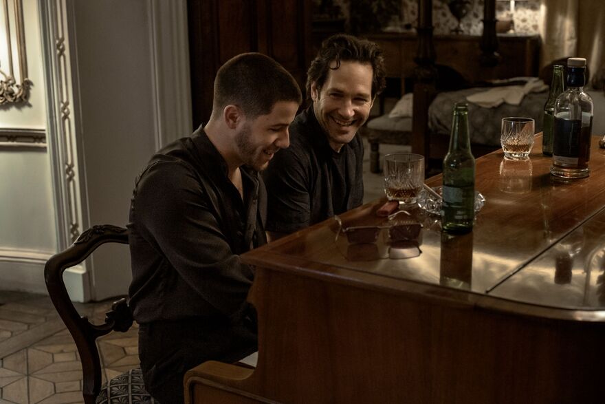 Two men sit together smiling at a piano. 