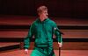 James Acaster in a green hoodie and sweatpants holding a microphone