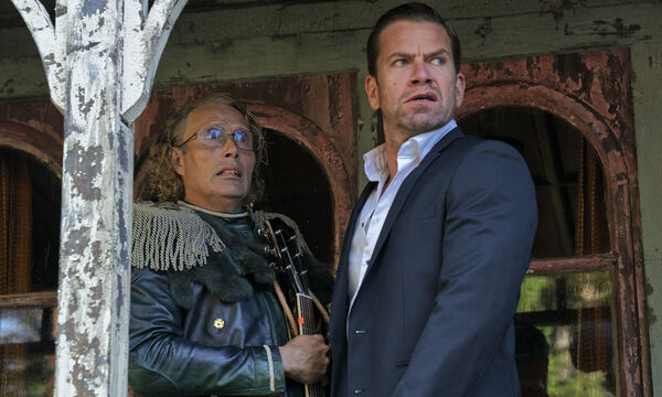 Two brothers stand together on a veranda looking alarmed. 