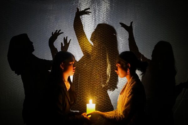 Two girls hold a candle as three others dance in the shadows behind them
