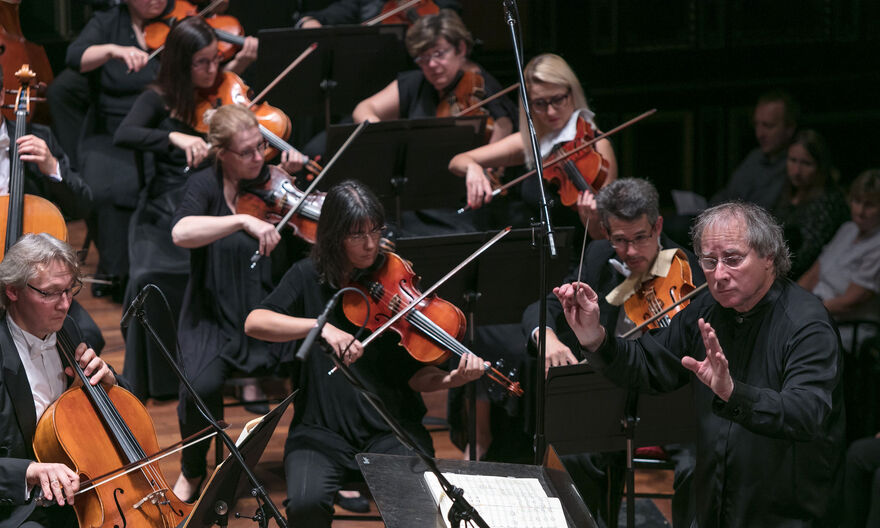 A group of musicians playing string instruments with a conductor