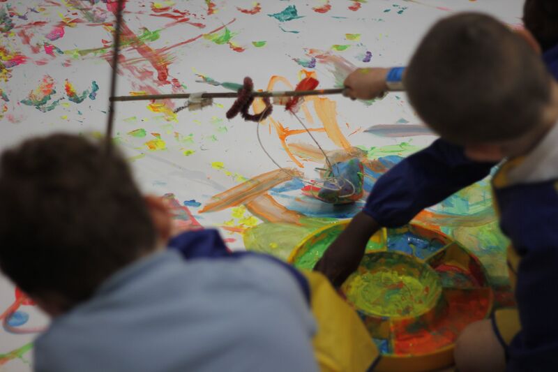 Children using paint on a big sheet of white paper 