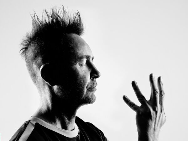 Nigel Kennedy with eyes closed and one hand up, image is in black and white