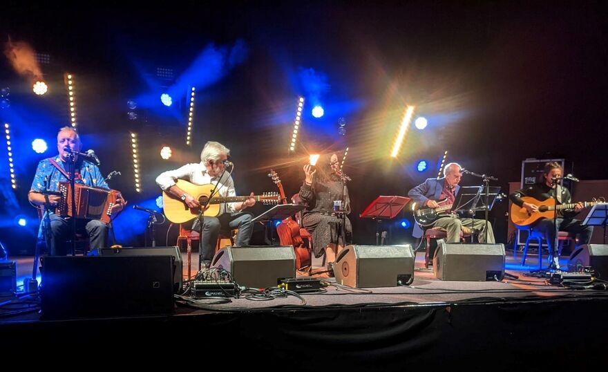 Band sat on chairs on stage with instruments by their side