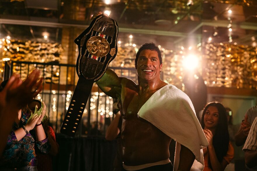 A man holds up a wrestling belt as people applaud.