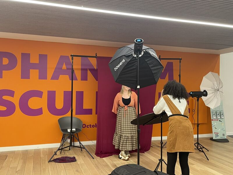 1.	Photographer Ayesha Jones taking a photograph of a participant at the We Just Click event at Warwick Arts Centre. The participant is stood in front of a burgundy backdrop.