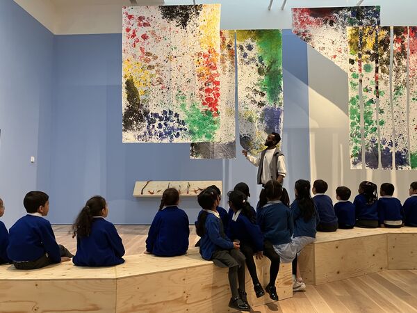School children sitting on wooden blocks in the mead gallery watching a man talking about paintings