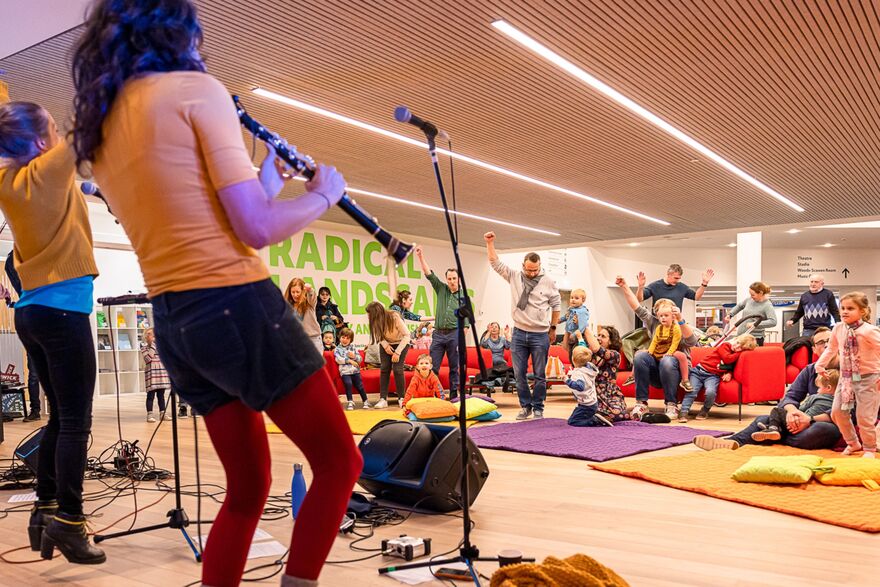 Musicians performing live on stage while children and families dance along on colourful mats.