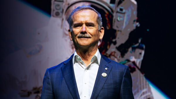 Chris Hadfield in a blue suit with an image of an astronaut behind