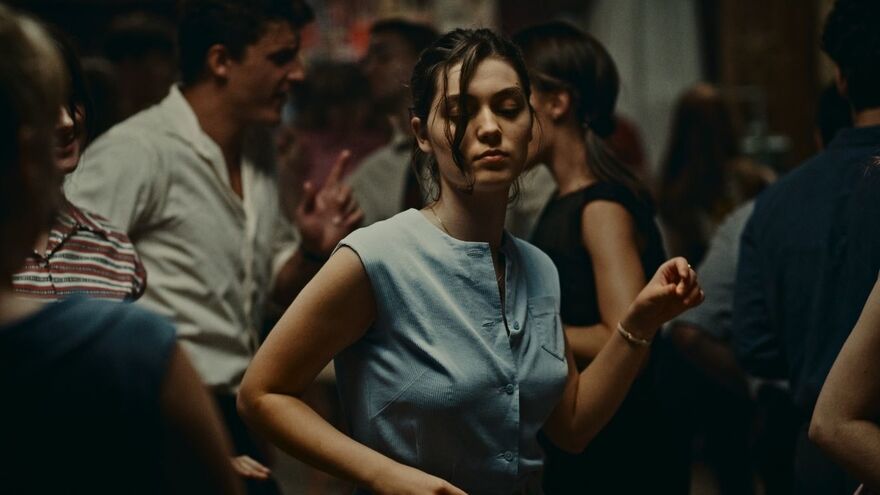 A young woman, wearing a blue top, dances alone with her eyes closed