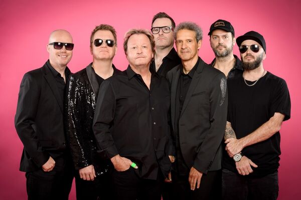 Full Band of Level 42 stood in black shirts with a pink background