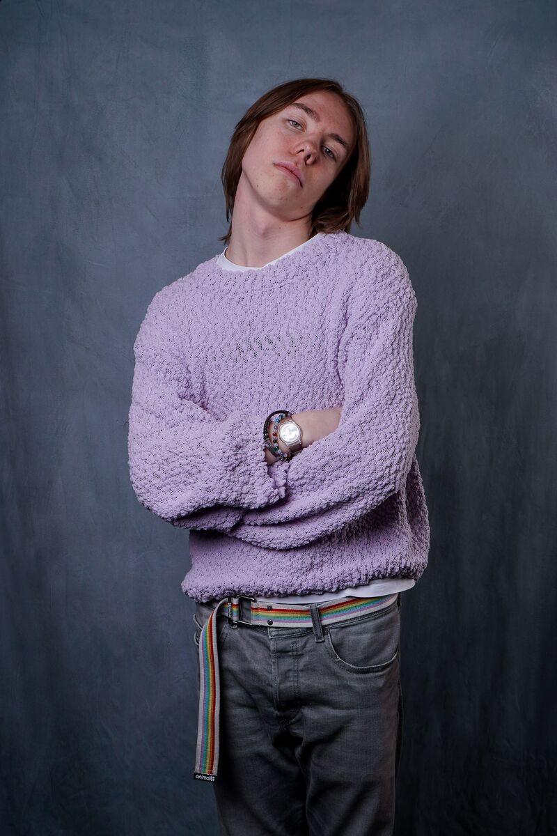 Boy wearing lilac fluffy sweater standing in front of a dark blue background