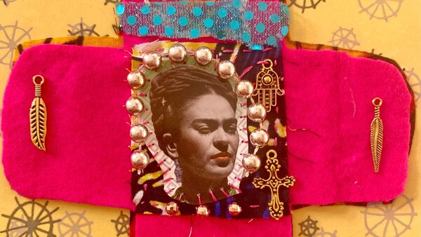 Handmade portable textile shrine with a portrait of Frida Kahlo, bead embroidery, and charms on pink fabric.