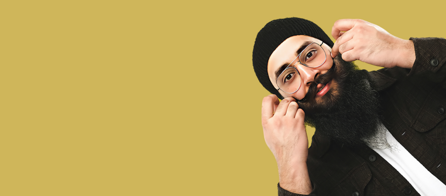 Preet stands with his hands by his moustache to the right side of the image, with a gold-yellow background