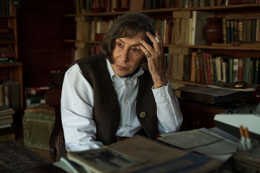 An older woman sits in a library holding her hand to her face. 