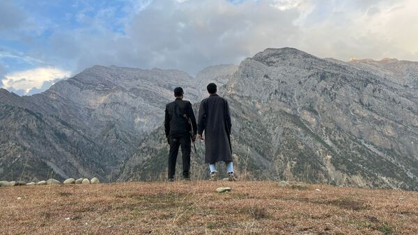 Two men stand side by side looking out over a mountainside. 