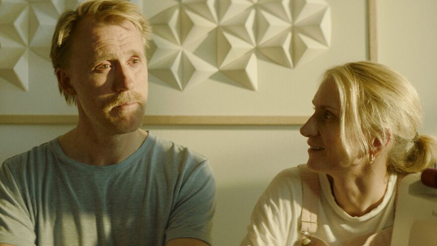 A woman looks at a man. He is looking to the side.