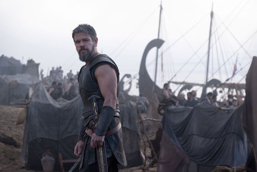 Matt Damon as Odysseus surrounded by boats on a beach. 
