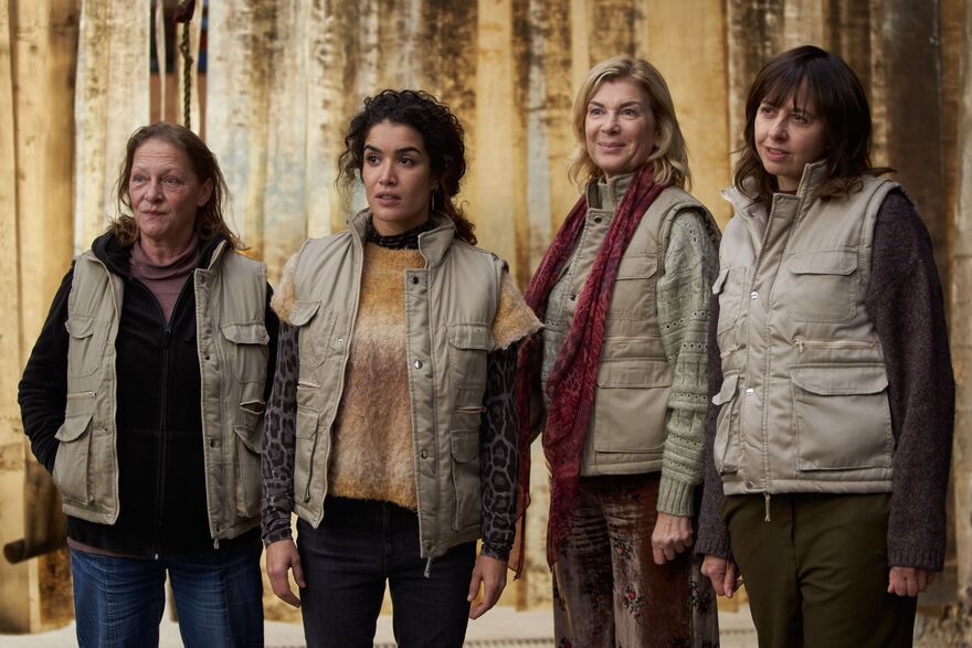 Four women stand next to each other. They are all wearing beige gilets.
