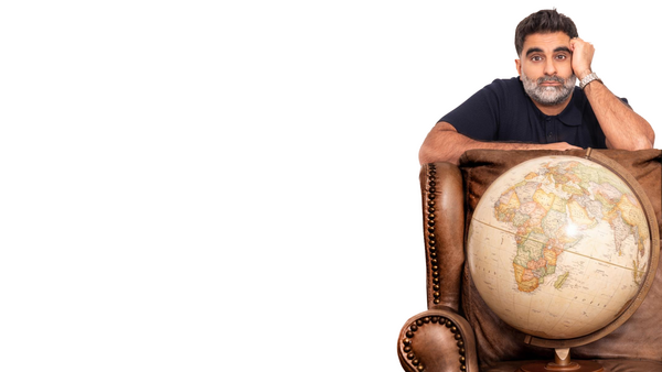 Comedian Tez Ilyas looking grumpy whilst leaning on a leather armchair behind a large vintage globe.