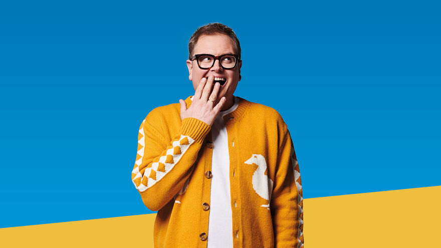 Alan Carr smiling with his hand to his mouth