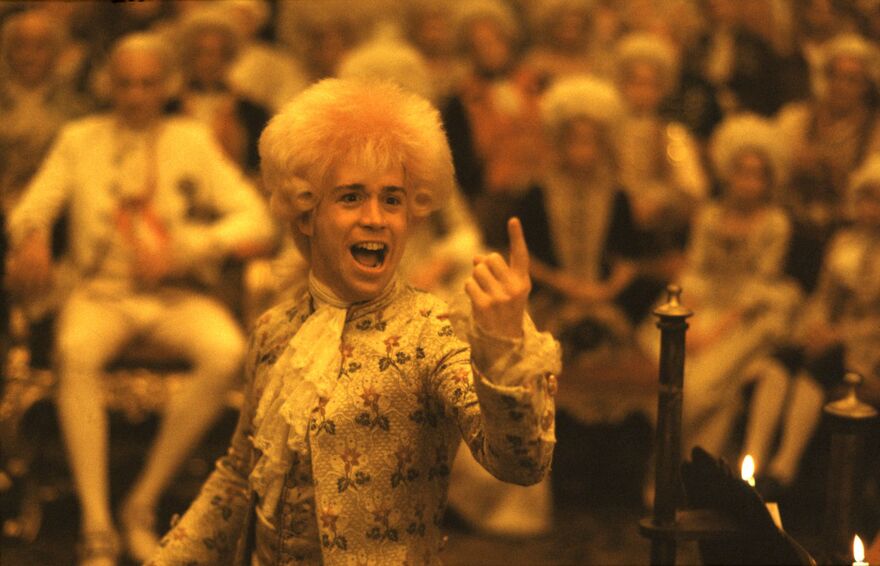 Tom Hulce as Wolfgang Amadeus Mozart. An audience can be seen in the background. 