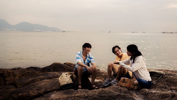 A group of friends sit together on rocks next to the sea. 