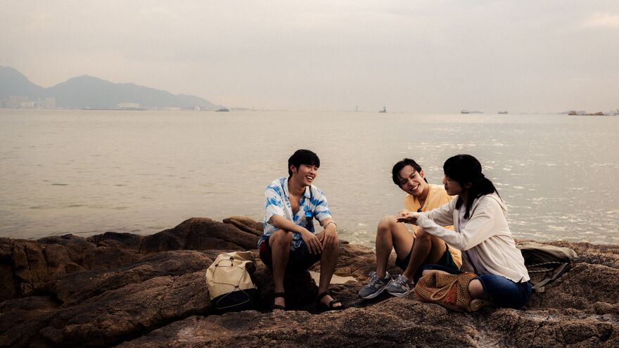 A group of friends sit together on rocks next to the sea. 