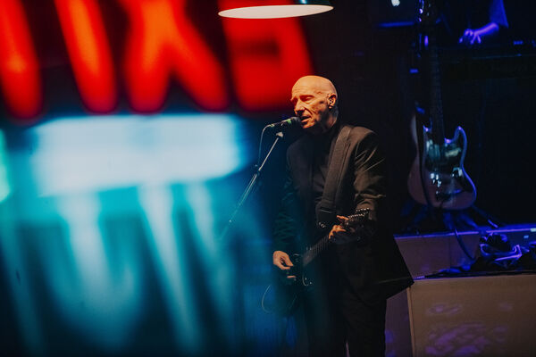 Midge Ure sings into the microphone whilst playing the guitar