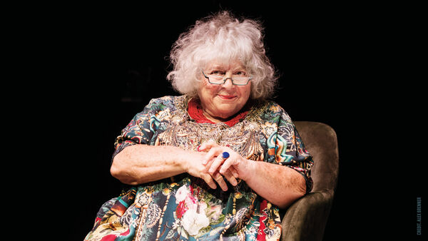 Miriam Margolyes in a colourful dress sat on an armchair